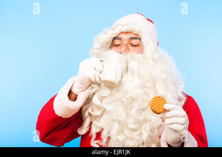 Santa Claus trinken aus einer Tasse Milch mit einem Keks in der hand Stockfoto