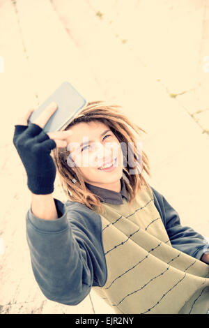 Porträt des jungen Kerl im Freien mit Rasta Haar Lächeln mit Smartphone in ein Lifestyle-Konzept mit einem warmen Filter angewendet Stockfoto