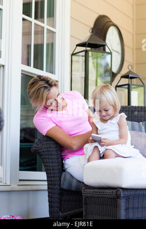 Kaukasische Mutter und Tochter mit Handy auf Veranda Stockfoto