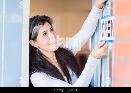 Hispanische Kleinunternehmer hängende Schild "geöffnet" auf Tür Stockfoto