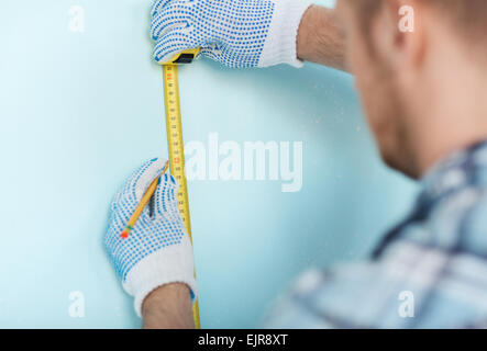 Nahaufnahme des Mannes in Handschuhen messen Wand mit Klebeband Stockfoto