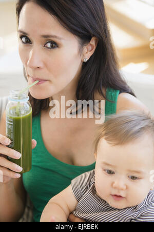 Nahaufnahme von Mischlinge Mutter hält Baby und grünen Saft trinken Stockfoto