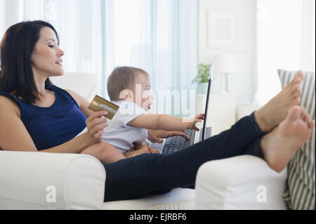 Mischlinge Mutter hält Baby und shopping auf laptop Stockfoto