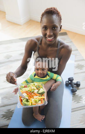 Schwarze Mutter hält Baby Boy und Salat essen Stockfoto