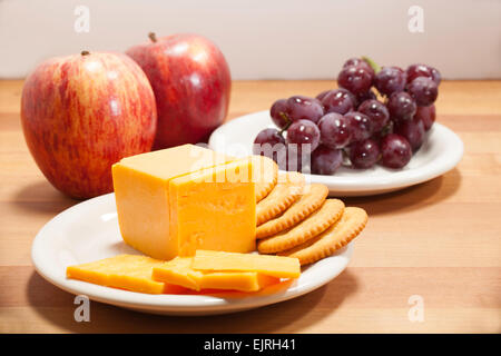 Gelbe Cheddar-Käse in Scheiben geschnitten auf einem weißen Teller mit Runde Cracker.  Eine weitere Platte rote kernlose Trauben sitzt in der staatlich Stockfoto