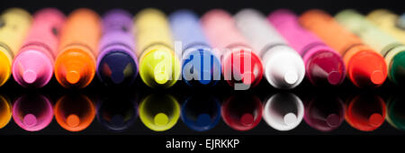 Ein Panorama-Format Bild mit verschiedenen farbigen Buntstiften auf eine glänzende schwarze Oberfläche reflektiert Stockfoto