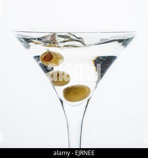 Ein Martini-Glas auf weißem Grund; das Wasser plätschert und spritzte wie eine grüne spanische Oliven mit Piment in gelöscht wird die Stockfoto