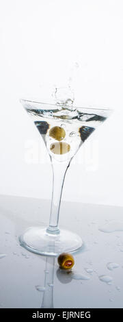 Ein Martini-Glas auf weißem Grund; das Wasser plätschert und spritzte wie eine grüne spanische Oliven mit Piment in gelöscht wird die Stockfoto