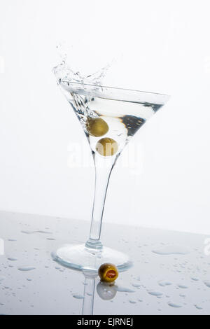 Ein Martini-Glas auf weißem Grund; das Wasser plätschert und spritzte wie eine grüne spanische Oliven mit Piment in gelöscht wird die Stockfoto