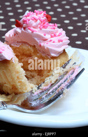 Ein gelber Kuchen Cupcake hat rosa Buttercreme Zuckerguss und rot, weiß und rosa besprengt; auf weißen Teller mit Gabel Stockfoto