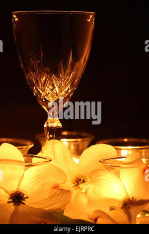 Eine Glas Weine ist beleuchtet werden nur Kerzenlicht.  Das weiche Licht scheint durch weiße Blumen in den Vordergrund gestellt. Stockfoto