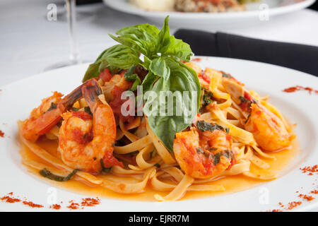 Ein weißer Teller hält Linguine mit Garnelen in Fra Diavolo Sauce, garniert mit frischem Basilikum. Paprika ist auf die Teller gestreut. Stockfoto