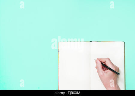 Hand mit leeren Notizblock und Stift auf blauem Hintergrund Stockfoto