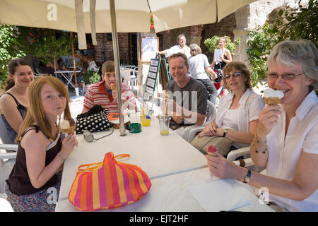 Familiengruppe sitzen an einem französischen Café-Tisch unter einem Sonnensegel Sonnenschirm genießen Eis Kornette. Stockfoto