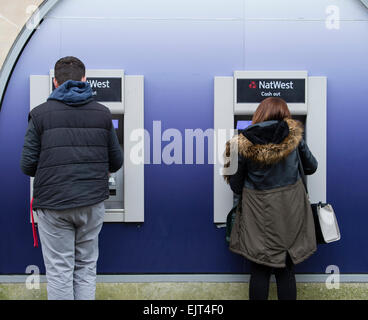 Zwei junge Menschen, die mit NatWest National Westminster Bank Geldautomaten Bargeld zeigen Maschinen, Swansea Wales UK Stockfoto