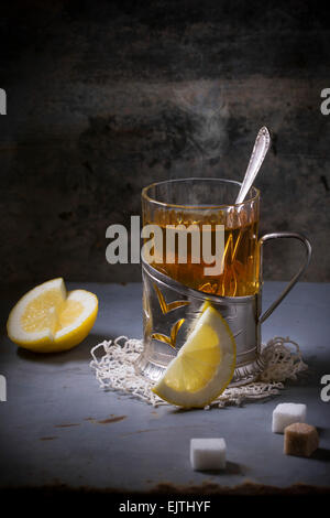 Vintage Glas-Halter auf gestrickte Serviette mit Tasse Tee mit in Scheiben geschnittenen Zitrone und Zucker Würfel über alten Metall-Tisch. Stockfoto