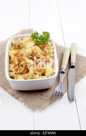 Käse-Spätzle mit gerösteten Zwiebeln und Petersilie in einer Schüssel weiß auf braun Jute mit Messer und Gabel Stockfoto