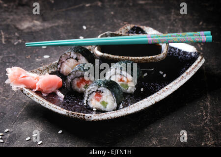 Sushi-Rollen mit Lachs, serviert auf schwarze Platte mit eingelegtem Ingwer, Sojasauce und türkisen Stäbchen auf dunklem Hintergrund. Stockfoto