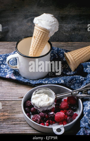 Hausgemachtes Vanilleeis in Wafer Kegel und leere Waffer Zapfen, serviert in Metallschale mit gefrorenen Beeren und Löffel über Holz Stockfoto