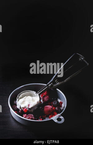 Aluminium-Platte mit Vanille-Eis und gefrorenen Beeren-Mix mit Metalllöffel über schwarzen Tisch serviert Stockfoto