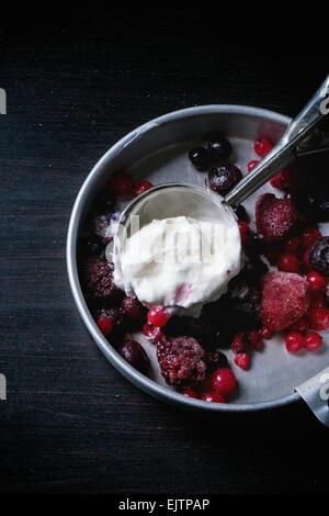 Aluminium-Platte mit Vanille-Eis und gefrorenen Beeren-Mix mit Metalllöffel über schwarzen Tisch serviert Stockfoto