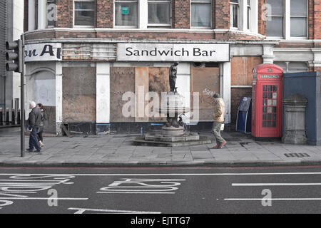 Fußgänger, vorbei an einem verlassenen Sandwichbar, box-Trinkbrunnen und Telefon in London. Stockfoto