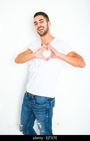 lässige schönen jungen Mann im weißen Hemd neben einer Wand Herzschild zeigt Stockfoto