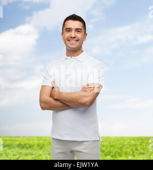 lächelnder Mann in weißem T-shirt mit verschränkten Armen Stockfoto