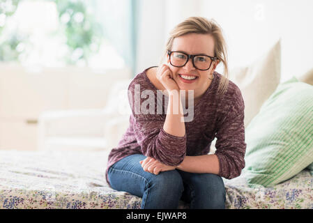 Porträt der lächelnde junge Frau sitzt auf Bett Stockfoto