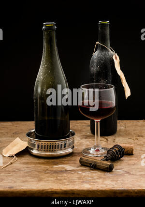 Stillleben mit Rotweinglas und Flaschen auf Holztisch, Studio gedreht Stockfoto