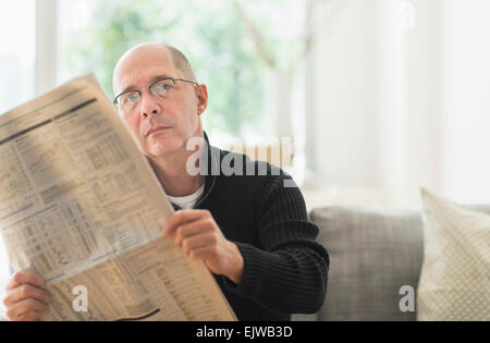 Reifer Mann liest Zeitung auf sofa Stockfoto