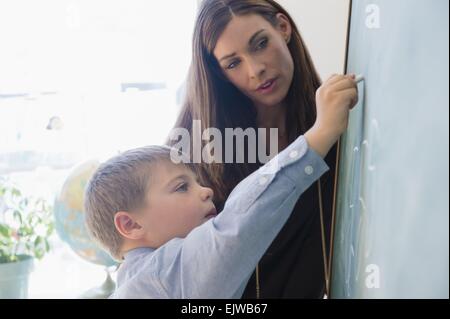 Lehrerin Schüler (6-7) während des Schreibens auf Tafel zu unterstützen Stockfoto