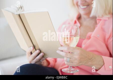 Ältere Frau Buch und Wein trinken Stockfoto