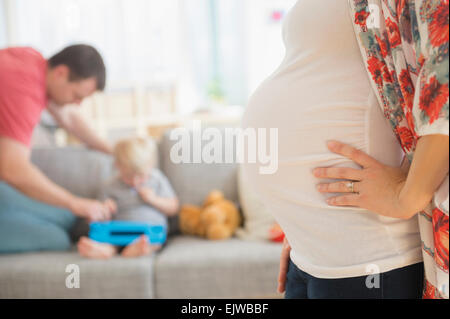 Anzeigen der schwangeren Frau im Wohnzimmer, Vater und Sohn (2-3) im Hintergrund Stockfoto