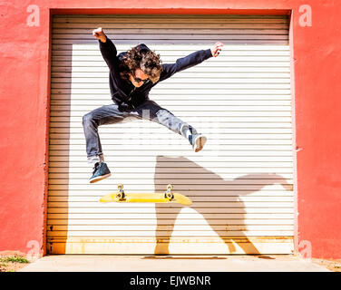 USA, Miami, West Palm Beach, Mann springt auf Skateboard gegen geschlossenen Garagentor Stockfoto