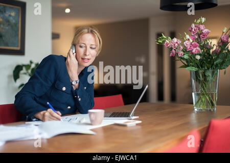 Frau am Telefon zu sprechen und sich Notizen macht Stockfoto