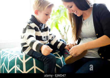 Mutter hilft Sohn (6-7) putting Schuh auf Stockfoto