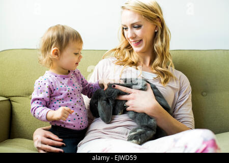 Mutter und Tochter (12-17 Monate) sitzt auf dem Sofa Kaninchen streicheln Stockfoto