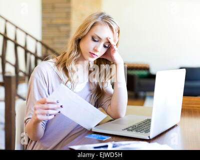 Junge Frau mit Laptop Blick auf Papier-Rechnung am Tisch sitzen Stockfoto