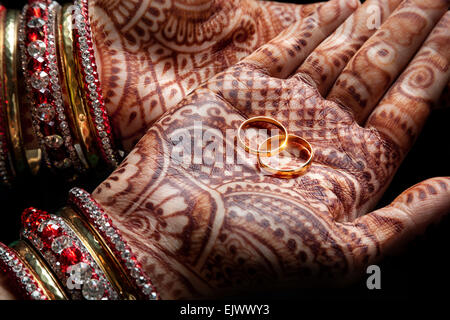 Frau Hände mit Henna halten zwei goldene Hochzeit Ringe auf schwarzem Hintergrund Stockfoto
