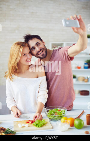 Glückliches junges Paar macht Selfie beim Kochen in der Küche Stockfoto