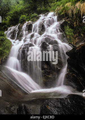 Lange Belichtung Wasserfall geschossen mit glatten Wasser läuft über brutale Felsen in leuchtenden grünen Wald. Medium Format vertikale Landschaft Stockfoto