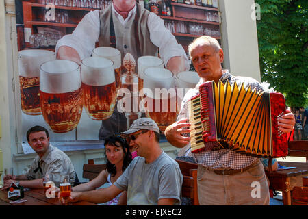 Prager Biergarten, Menschen trinken Bier Tschechische Republik Tourismus Prag Musiker Mann spielt Akkordeon für Menschen in einem Gartenrestaurant Stockfoto