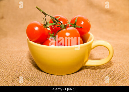 Cherry-Tomaten in eine gelbe Tasse auf alten Lappen Stockfoto