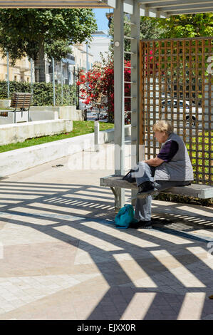 Ältere Dame sitzt auf einer Bank in einem öffentlichen Park. Stockfoto