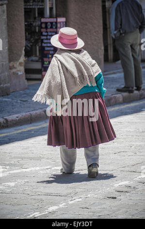Eine Person in traditioneller Andenkleidung läuft an einem sonnigen Tag in Cuenca Ecuador eine Kopfsteinpflasterstraße in einer kleinen Stadt entlang Stockfoto