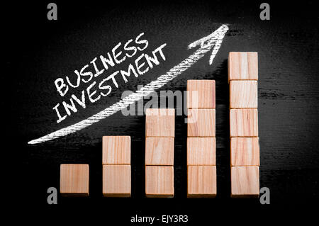 Wörter Unternehmensinvestitionen in aufsteigender Pfeil oben Balkendiagramm der hölzerne kleine Würfel auf schwarzem Hintergrund isoliert. Kreidezeichnung auf Tafel. Firmen-Konzept-Image. Stockfoto