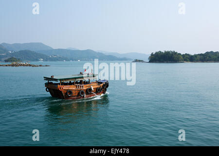 Kleines traditionelles Chinesisch Boot verlassen ein Fischerdorf in Hongkong, Reisen in Richtung Inseln über ein ruhiges Meer verlassen ein Weckruf an die Oberfläche. Stockfoto
