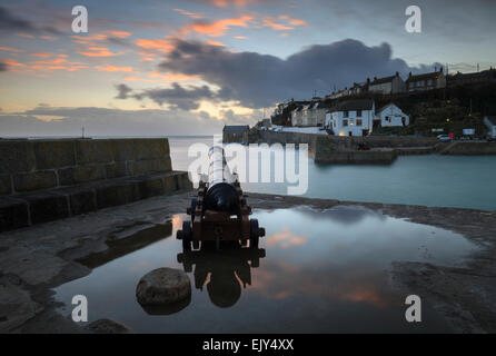 Eine Canon am Eingang zum Hafen von Porthleven auf Cornwalls Lizard Halbinsel, spiegelt sich in einem großen Wasserbecken. Stockfoto