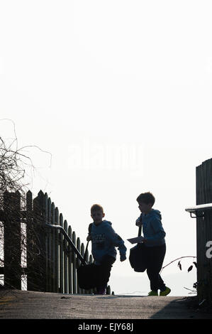 Zwei junge Grundschule Alter der Kinder (jungen) in der Silhouette, die zu Fuß zur Schule an einem kalten Wintermorgen, Wales UK Stockfoto
